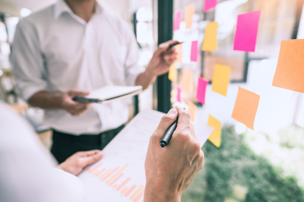 Business people meeting at office and use sticky notes on glass wall in office, diverse employees people group planning work together brainstorm strategy.